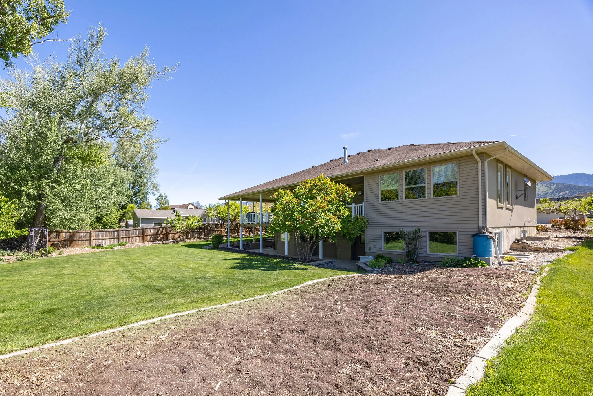 Expansive rear exterior featuring a covered patio, multiple large windows, a generous lawn area, and tiered landscaping beds