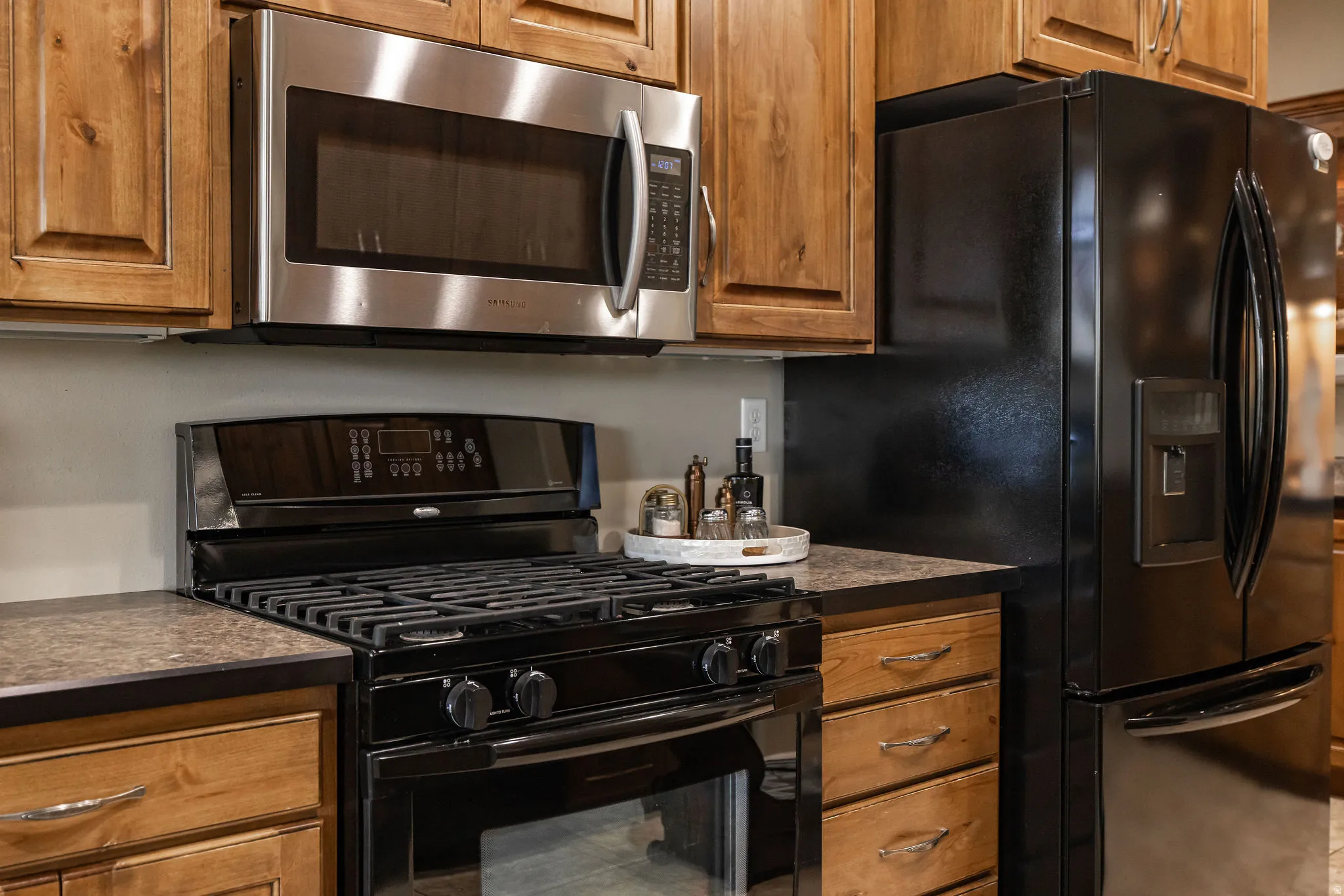 Kitchen featuring a stainless steel microwave, black gas range, black French door refrigerator with exterior dispenser, wood cabinetry, and dark countertops