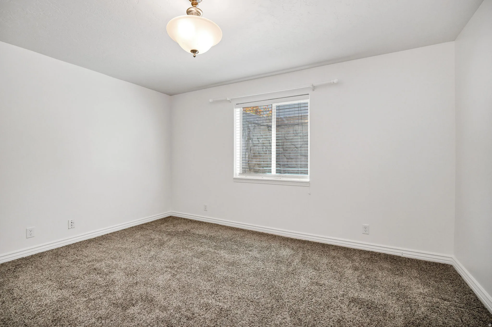 Bright interior space featuring neutral tone walls, a single window with blinds, and a flush mount ceiling light fixture