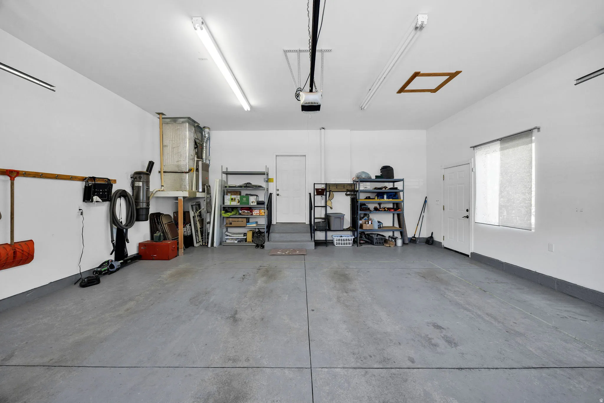Spacious garage featuring concrete flooring, multiple fluorescent lighting fixtures, and a garage door opener