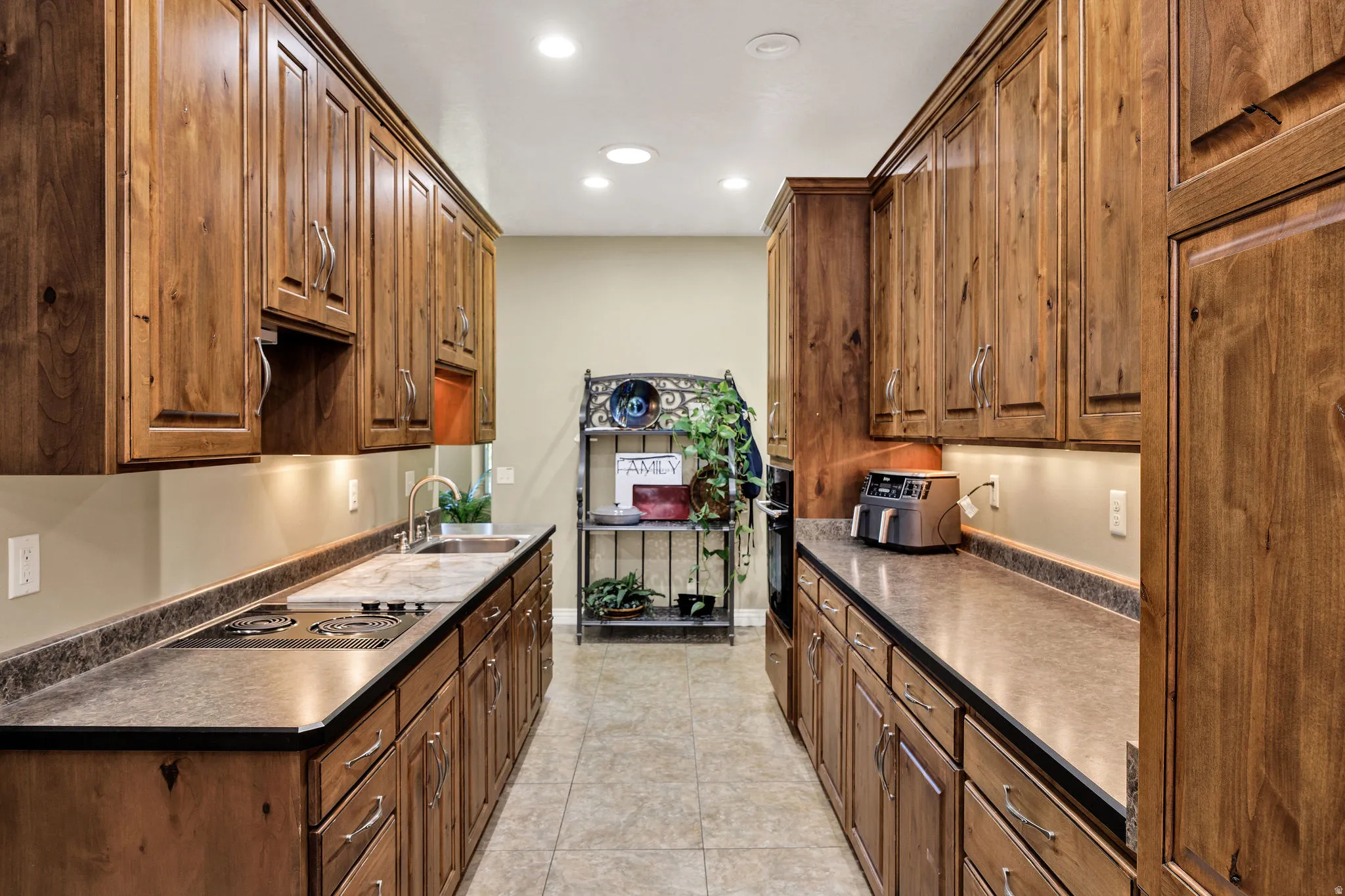Galley kitchen featuring extensive wood cabinetry, stone-finish countertops, recessed ceiling lighting, under-cabinet illumination, and tile flooring