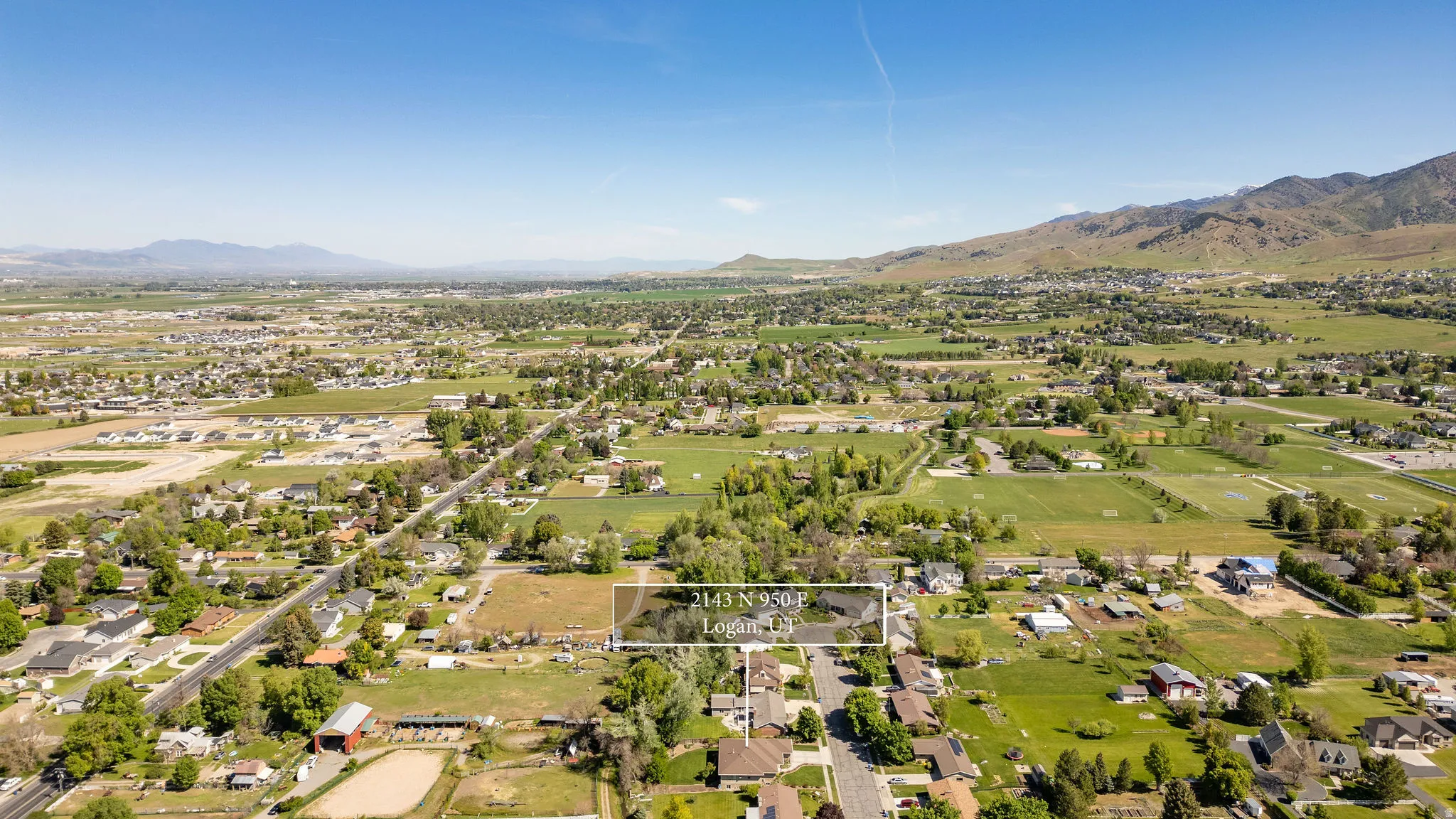 Expansive aerial showcasing a residential area amidst verdant fields and distant mountains