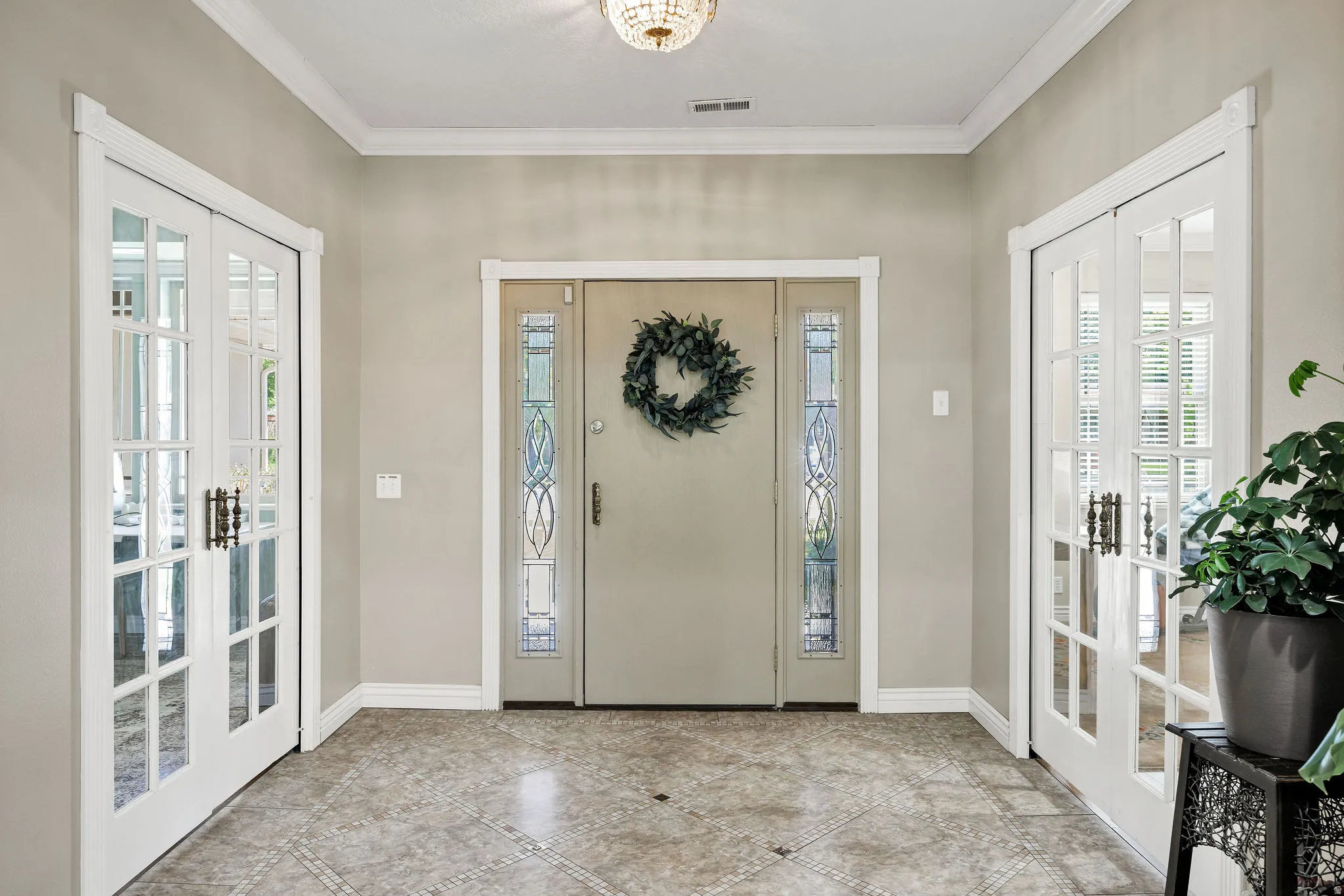 Foyer with patterned tile flooring, a central entry door with decorative glass sidelights, and two sets of interior French doors