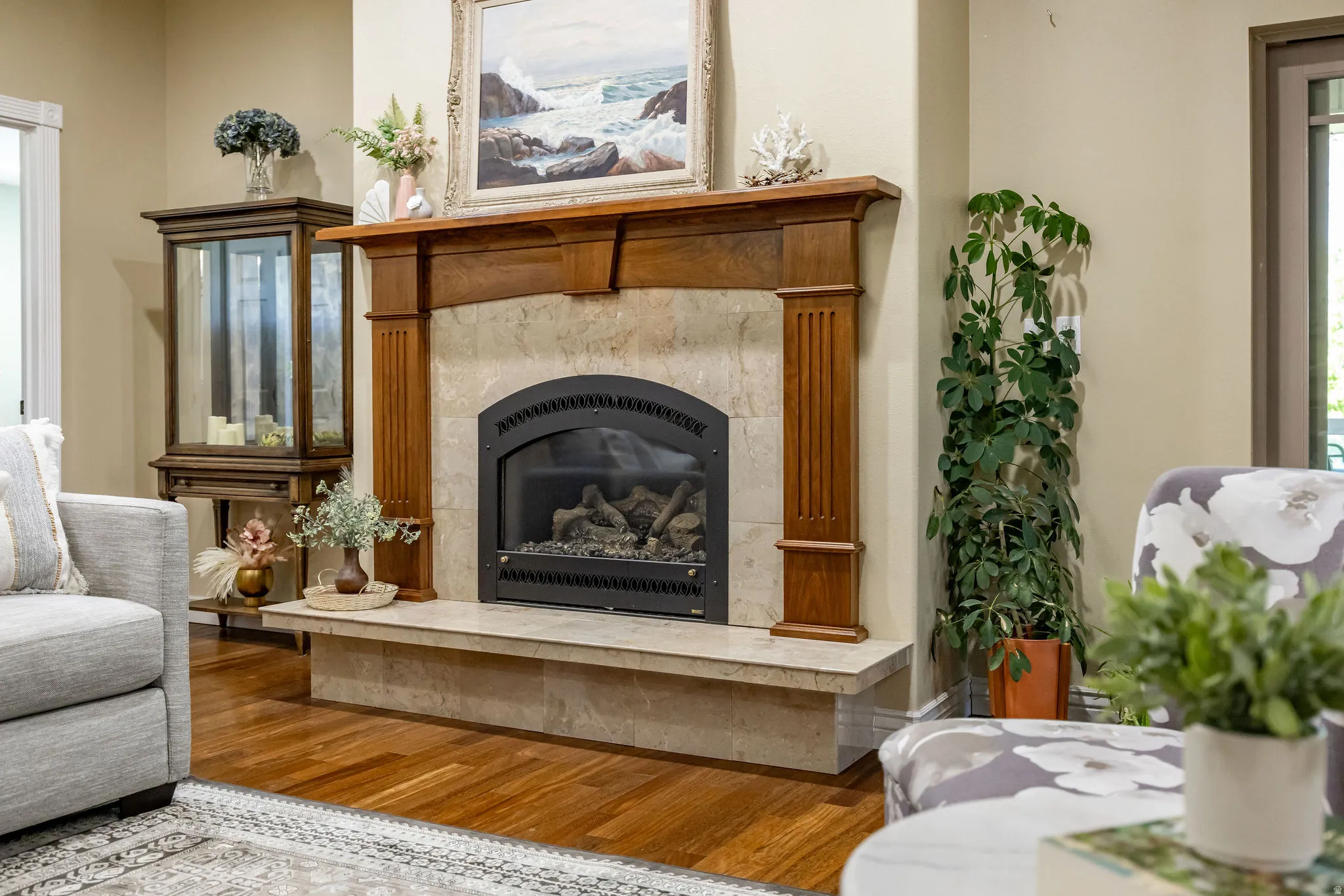 Gas fireplace with a black arched insert, stone surround, wood mantel, and wood-finish flooring