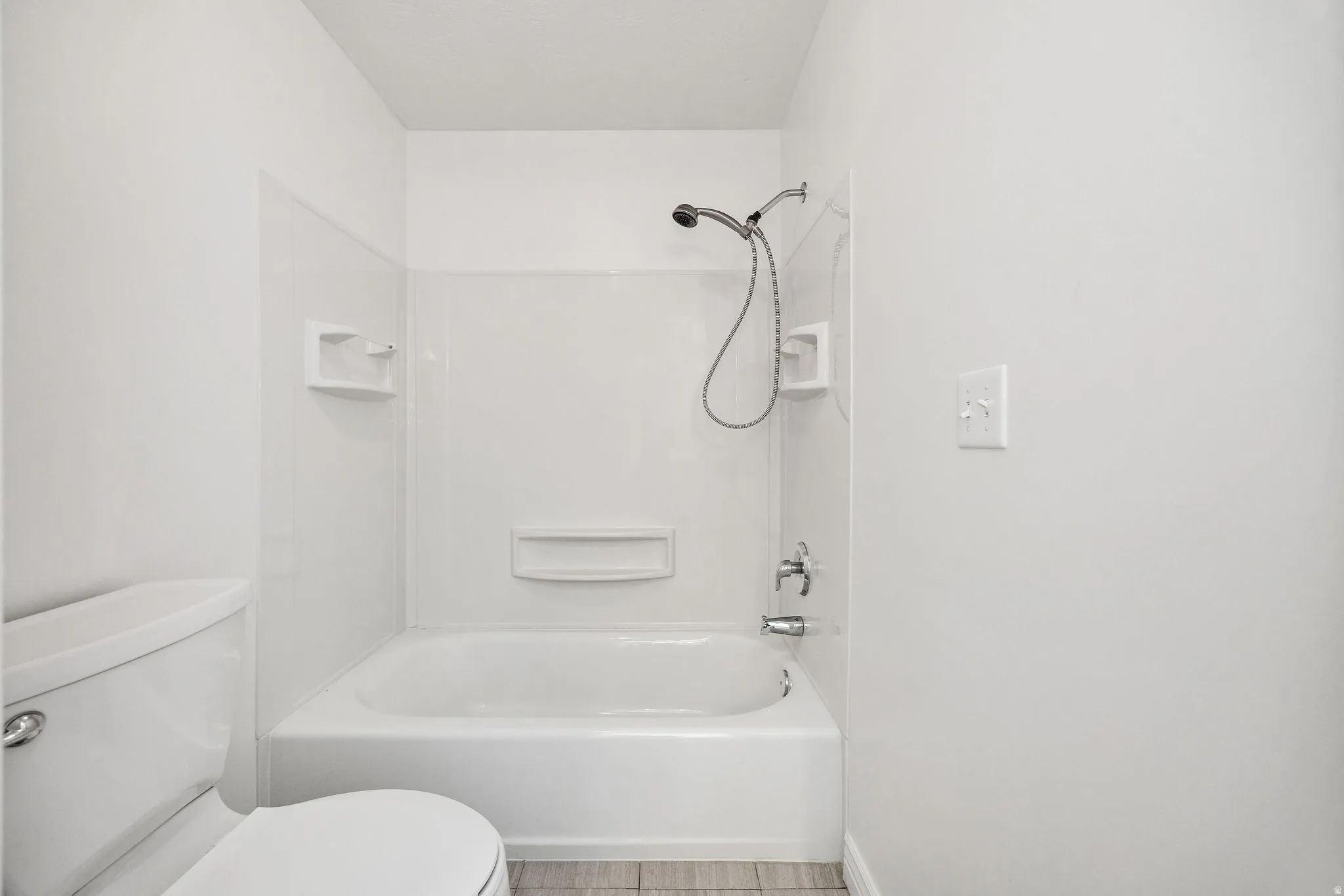 White bathtub with integrated shower, chrome fixtures, and a white tile-look surround