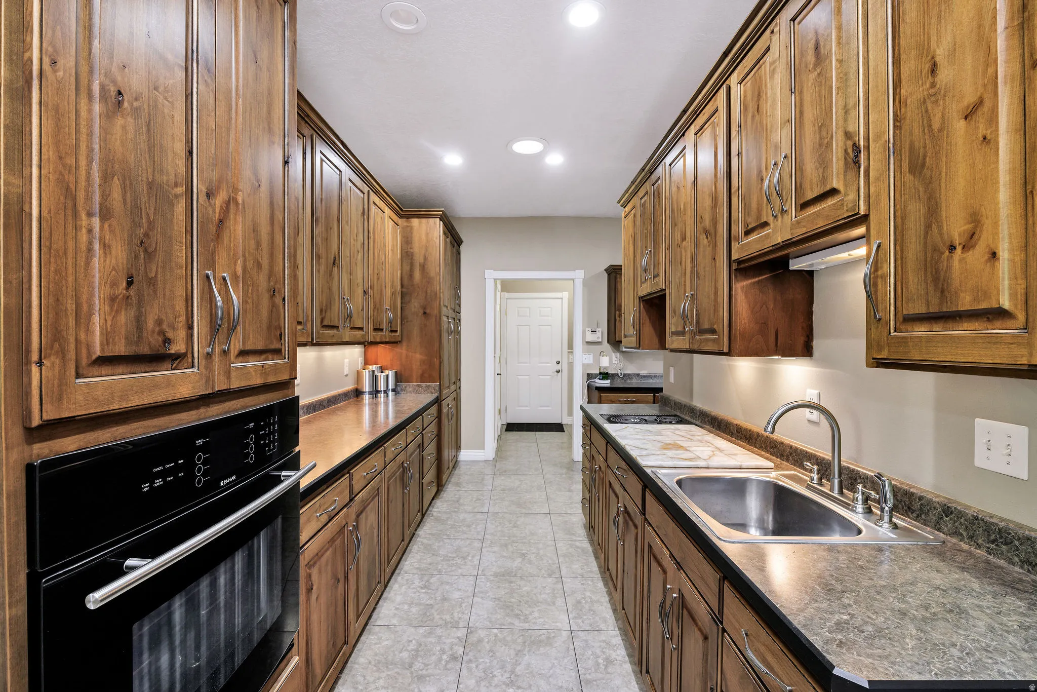 Galley kitchen featuring extensive wood cabinetry, recessed lighting, integrated wall oven, stainless steel sink, and tile flooring