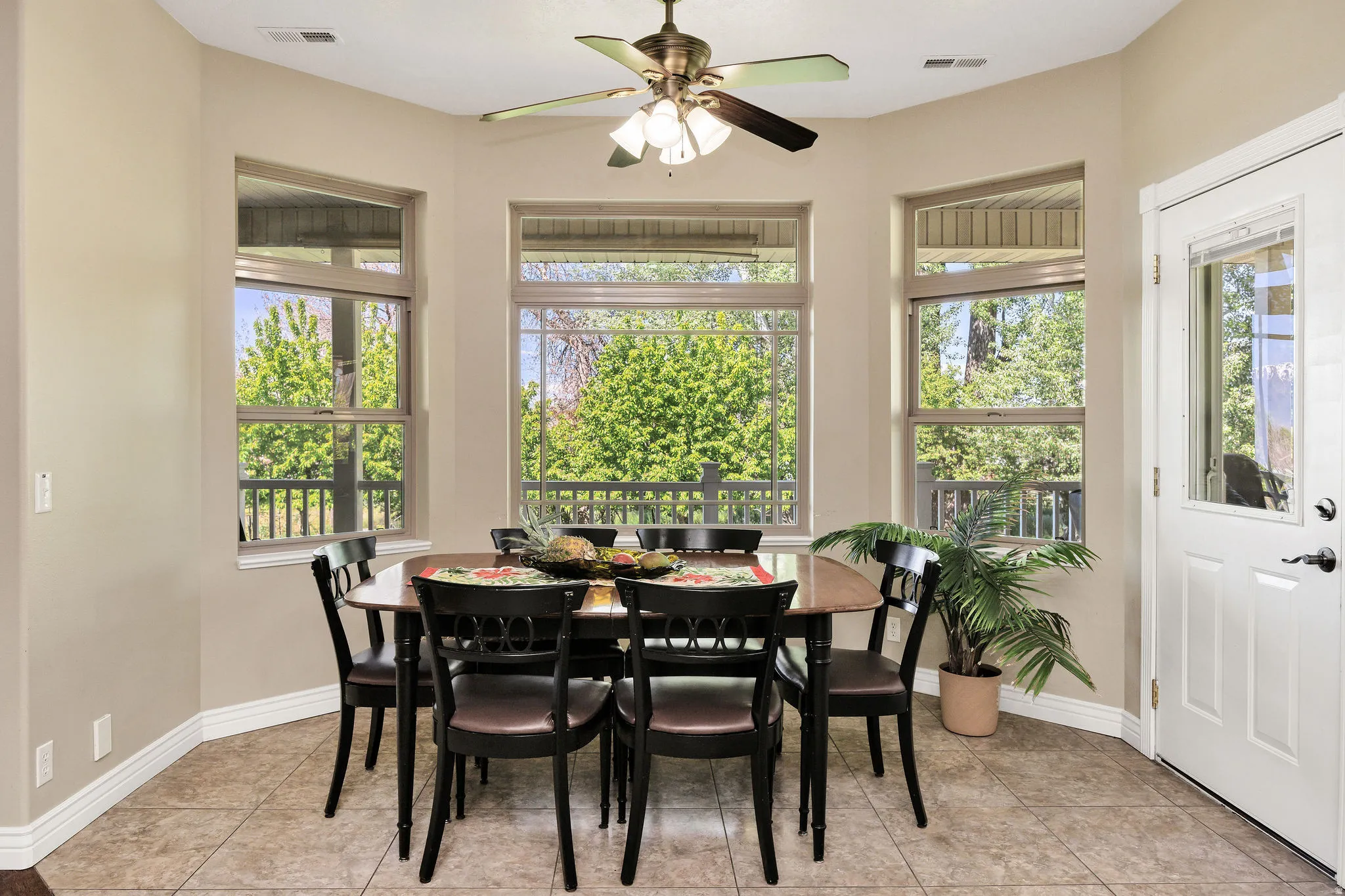 Dining area featuring a bay window with three large windows, tile flooring, a ceiling fan with integrated lighting, and a white paneled door with a half-light insert