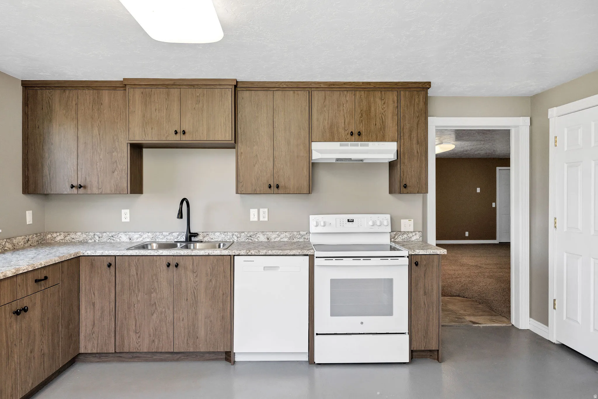 Kitchen featuring wood-finish cabinetry, granite-look countertops, a stainless steel double basin sink with a black gooseneck faucet, a white electric range, and a white dishwasher