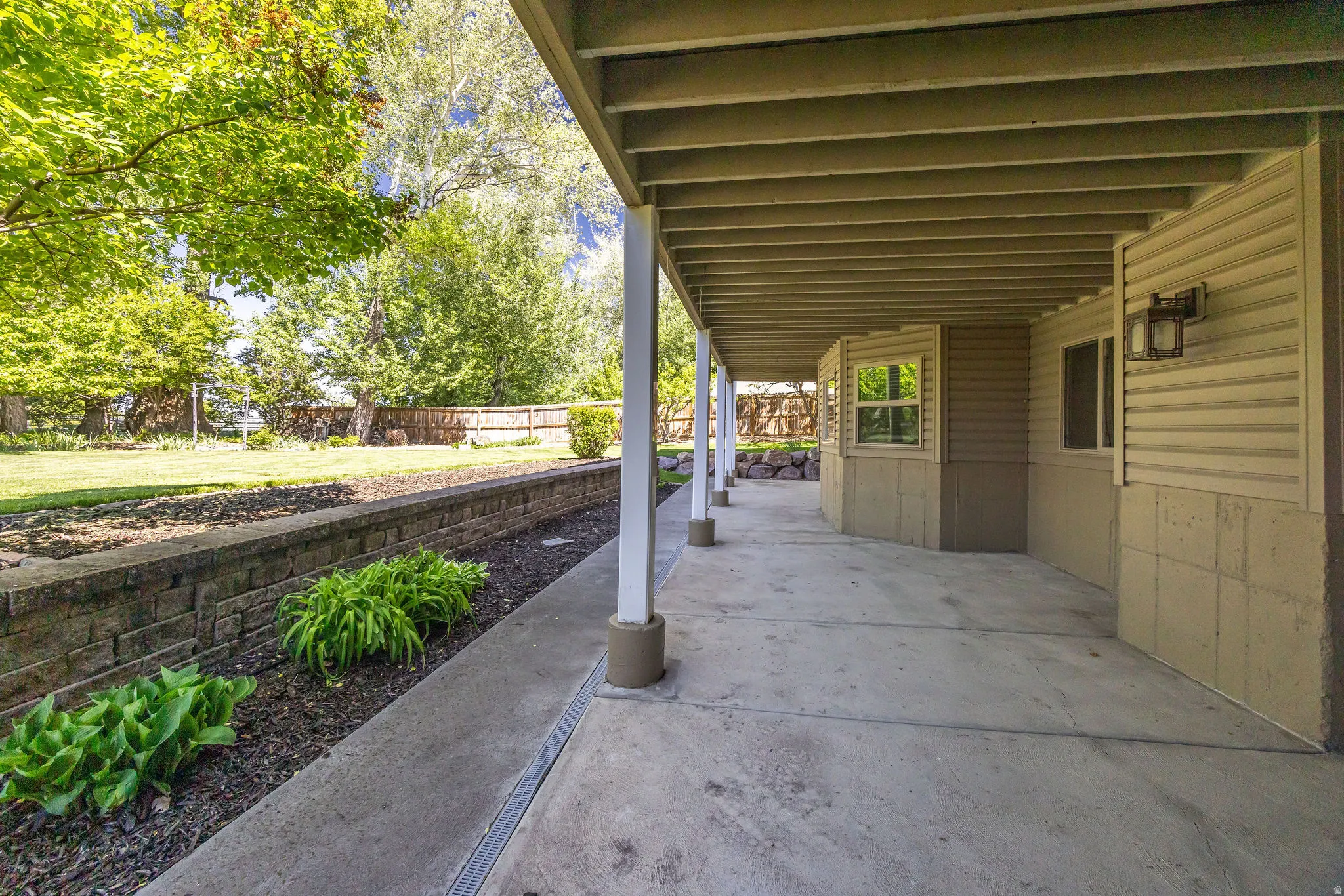 Expansive concrete patio with a covered ceiling, supported by white columns, offering an outdoor extension of the home