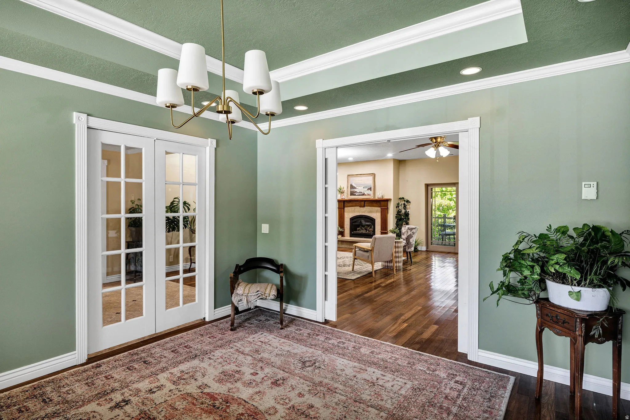 Room featuring a tray ceiling with recessed lighting and a brass chandelier, a wide entryway, and white French doors