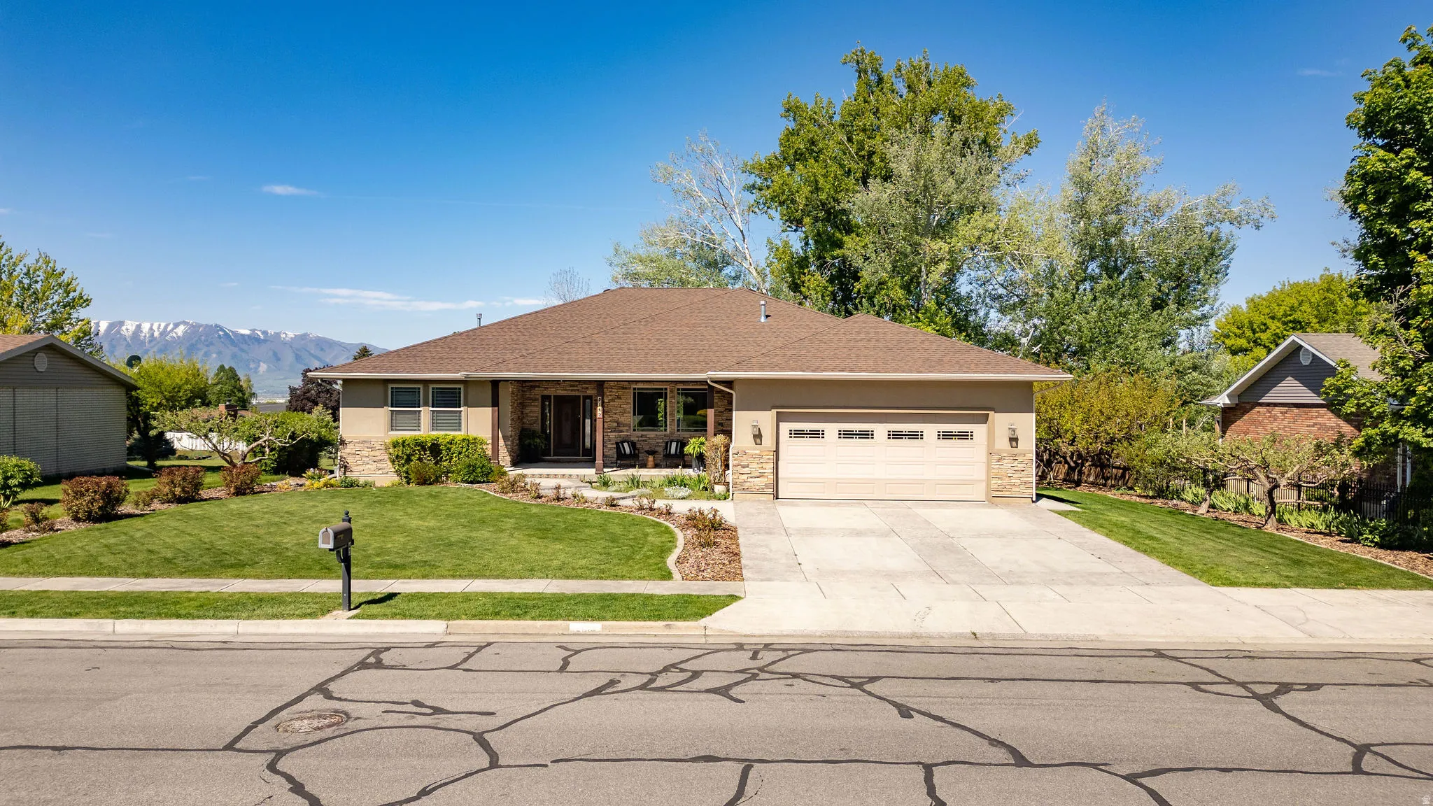 Ranch-style residence featuring a stone and stucco exterior, an attached two-car garage, a concrete driveway, and a front lawn with established landscaping