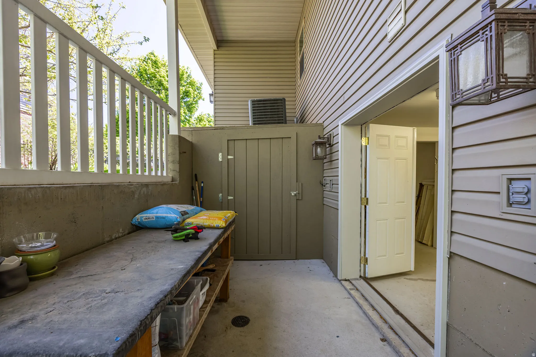 Covered concrete patio featuring white railing, built-in storage unit with matching exterior lighting, and a utility door