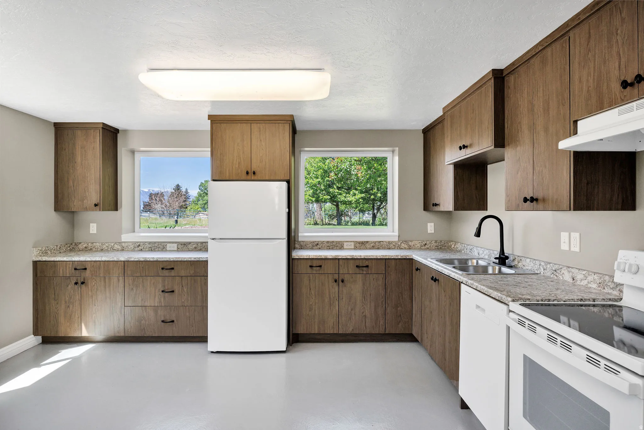 Spacious kitchen featuring wood-finish cabinetry, light-toned countertops, and a full suite of white appliances
