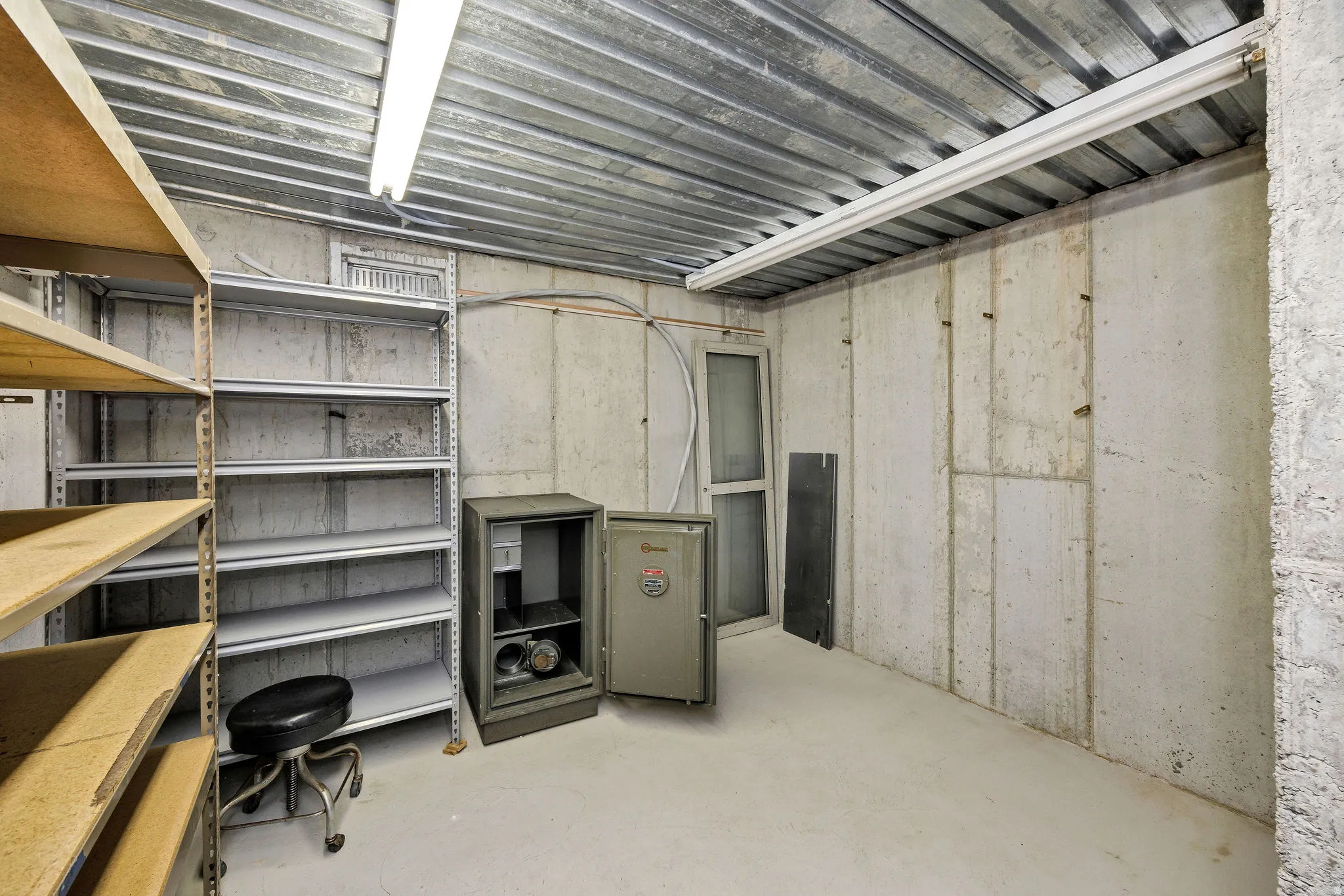 Utility room featuring concrete panel walls, a corrugated metal ceiling, and fluorescent strip lighting