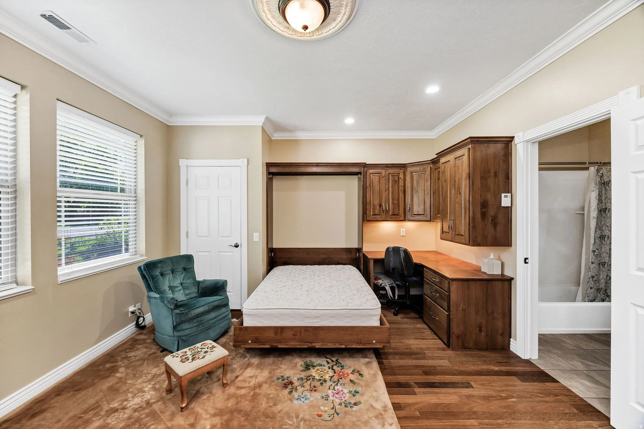 Room featuring a built-in wood desk with overhead cabinetry, a wall-mounted bed frame, and wood-finish flooring