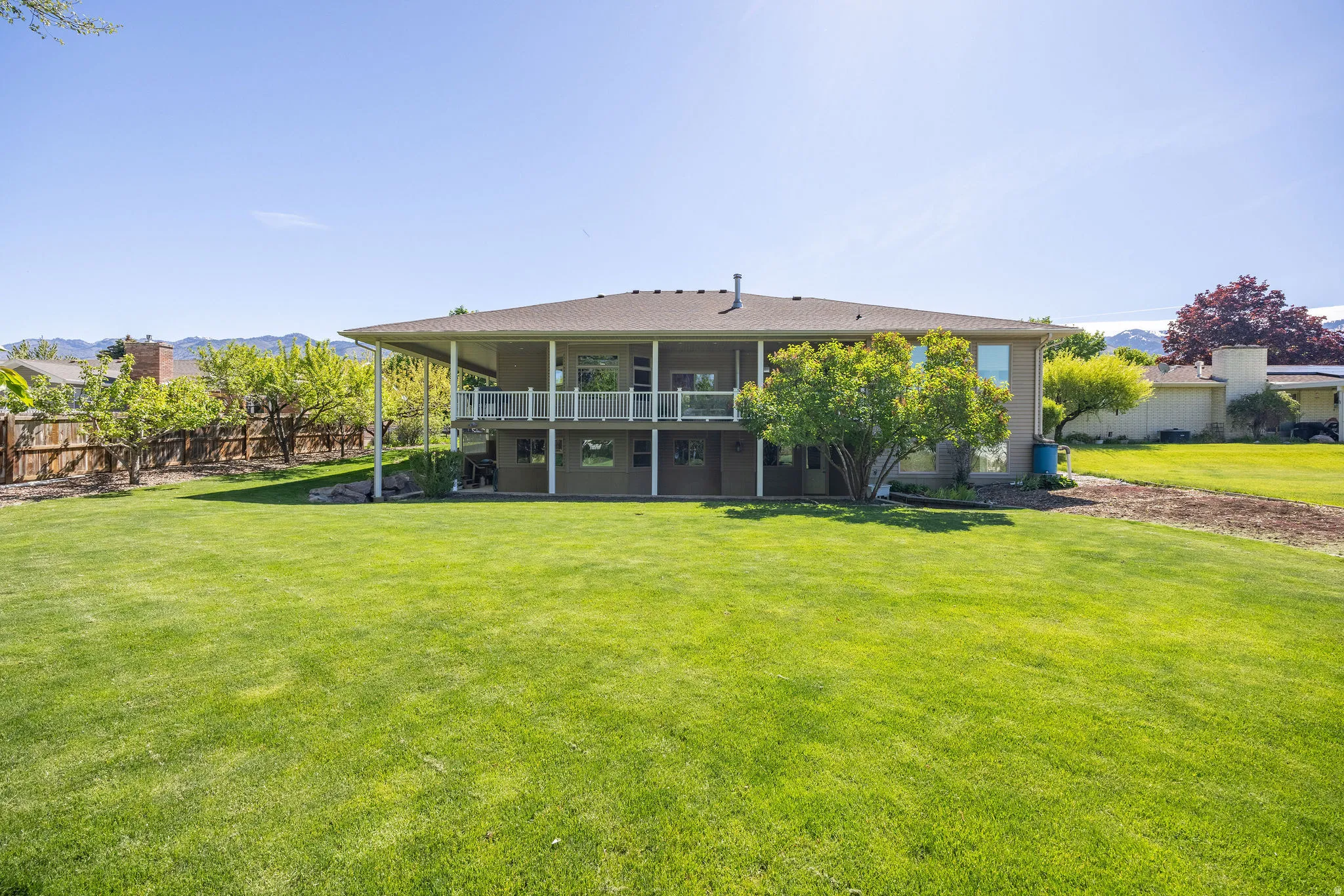 Expansive green lawn with a two-story residence featuring a covered upper-level balcony and a covered lower-level patio