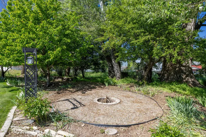 Outdoor fire pit area with gravel groundcover, surrounded by mature trees and lush green foliage