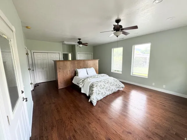 Spacious room featuring rich wood-finish flooring, multiple windows with blinds, and recessed lighting