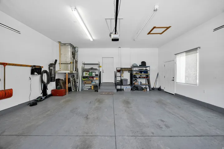 Spacious garage featuring concrete flooring, multiple fluorescent lighting fixtures, and a garage door opener