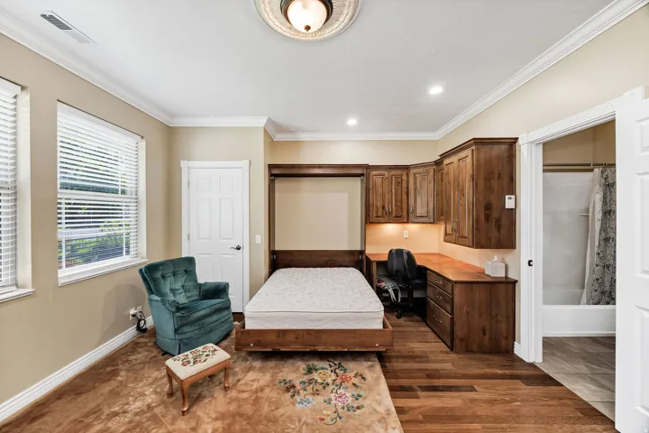 Room featuring a built-in wood desk with overhead cabinetry, a wall-mounted bed frame, and wood-finish flooring