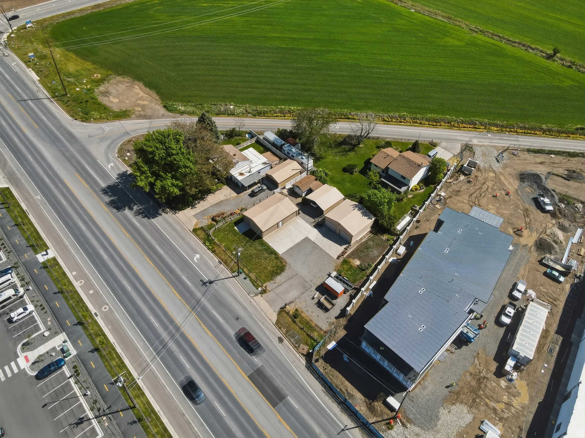 Aerial perspective showcasing a property with extensive paved areas, multiple detached garages, a two-story residence, and proximity to a large green field