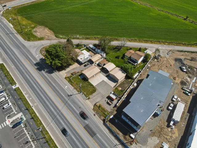 Aerial perspective showcasing a property with extensive paved areas, multiple detached garages, a two-story residence, and proximity to a large green field