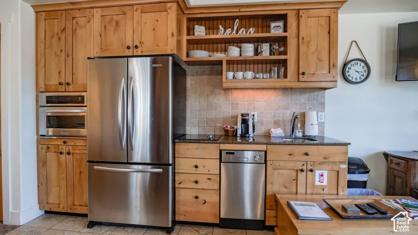 Compact kitchen area featuring natural wood cabinetry, stainless steel refrigerator, and integrated dishwasher