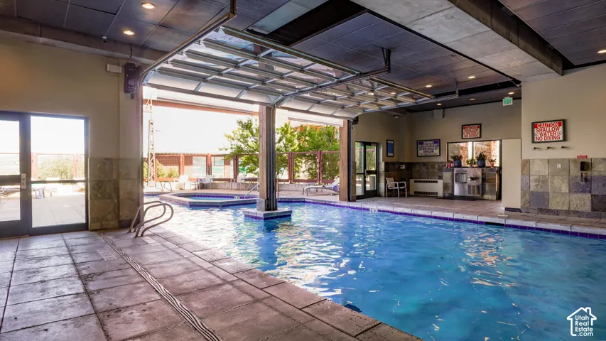 Indoor swimming pool with concrete decking, a transparent overhead door, and an integrated spa