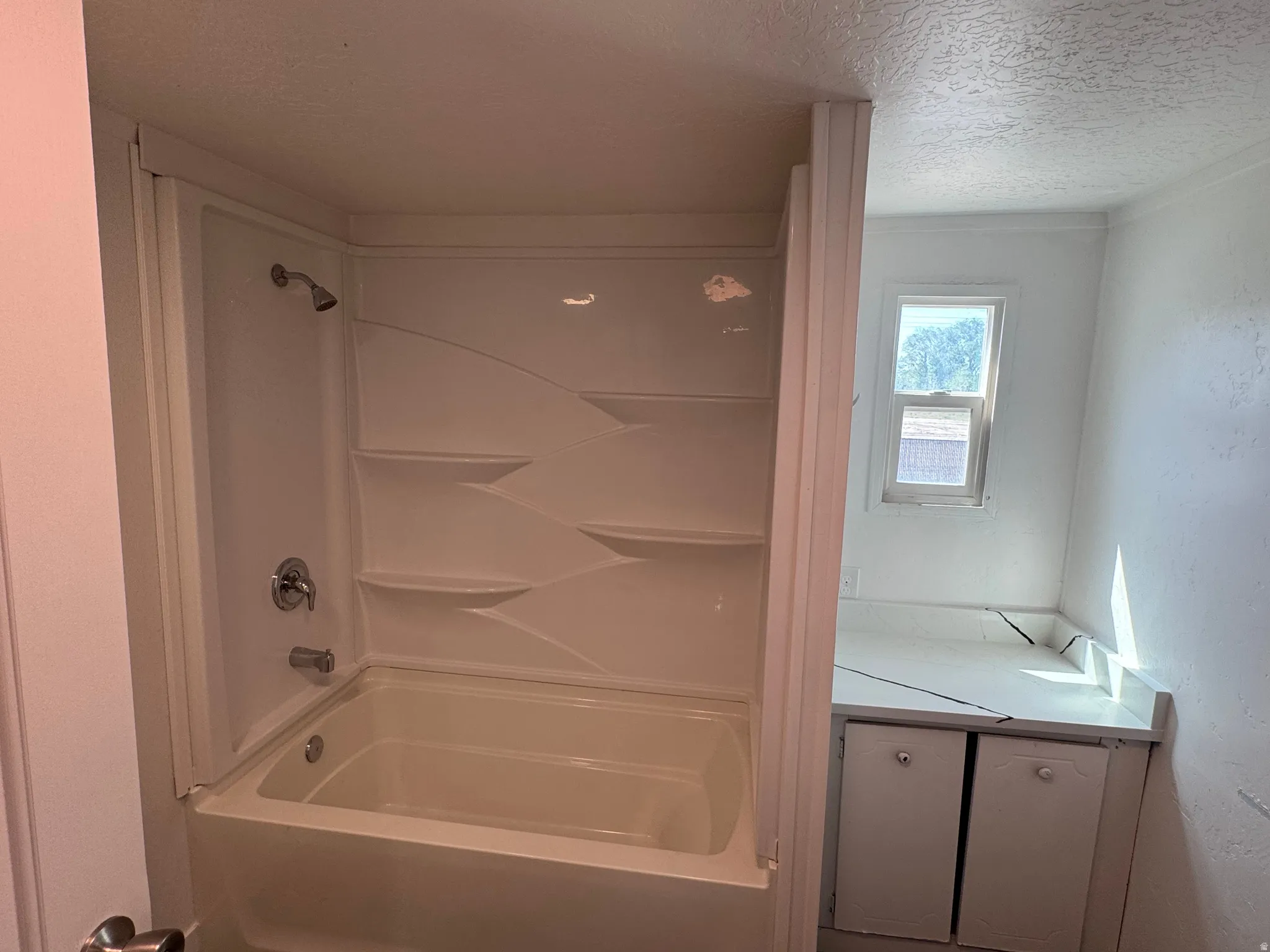 Bathroom featuring a white tub-shower combination with integrated shelving, chrome fixtures, and an adjacent built-in vanity with under-counter storage