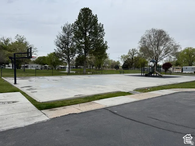 Recreational area featuring a basketball court, playground equipment, and mature trees