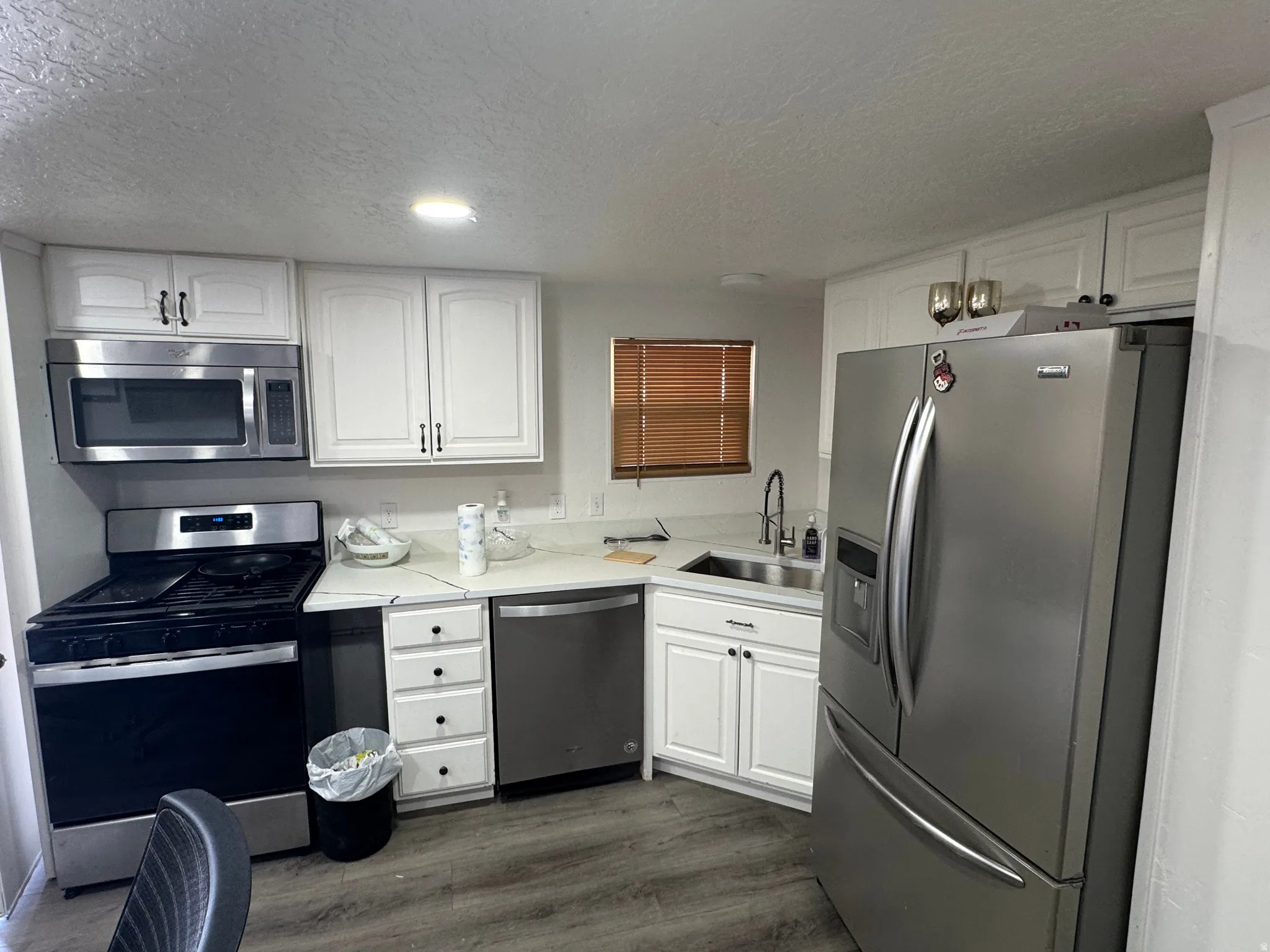 Kitchen featuring white cabinetry, light countertops, wood-finish flooring, and stainless steel appliances including a refrigerator, dishwasher, microwave, and range
