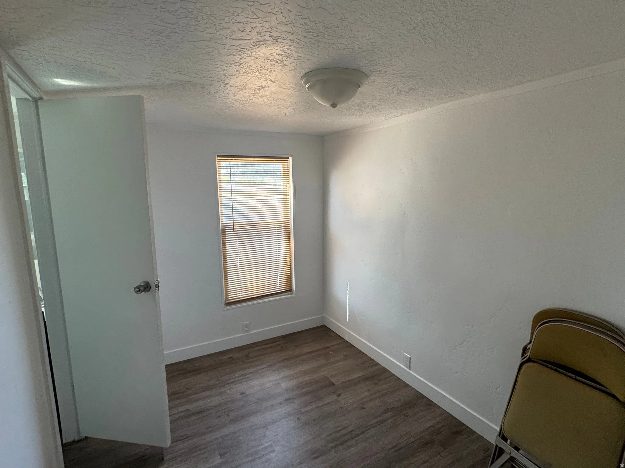 Room featuring wood-finish flooring, white baseboards, and a single window with blinds