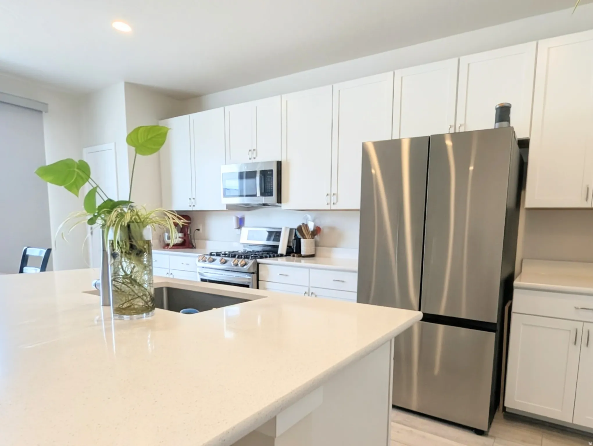 Bright kitchen featuring an island with an undermount sink, white cabinetry, stainless steel appliances, a gas range, and light-toned countertops
