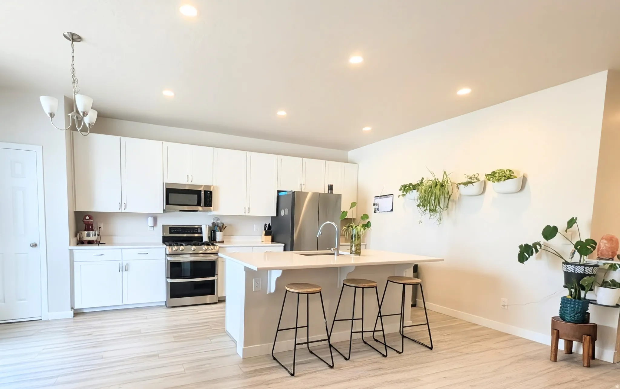 Kitchen featuring a central island with countertop seating, stainless steel appliances, white cabinetry, recessed lighting, and wood-finish flooring