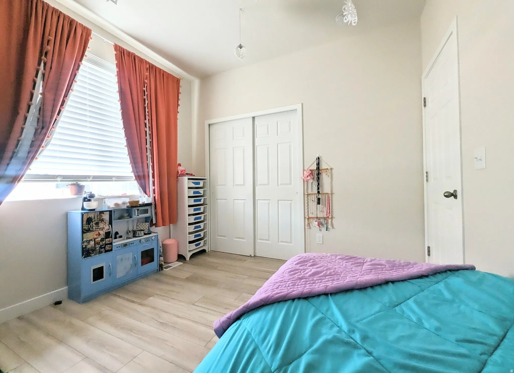 Spacious room featuring wood-finish flooring, light-toned walls, and a window with horizontal blinds and drapery