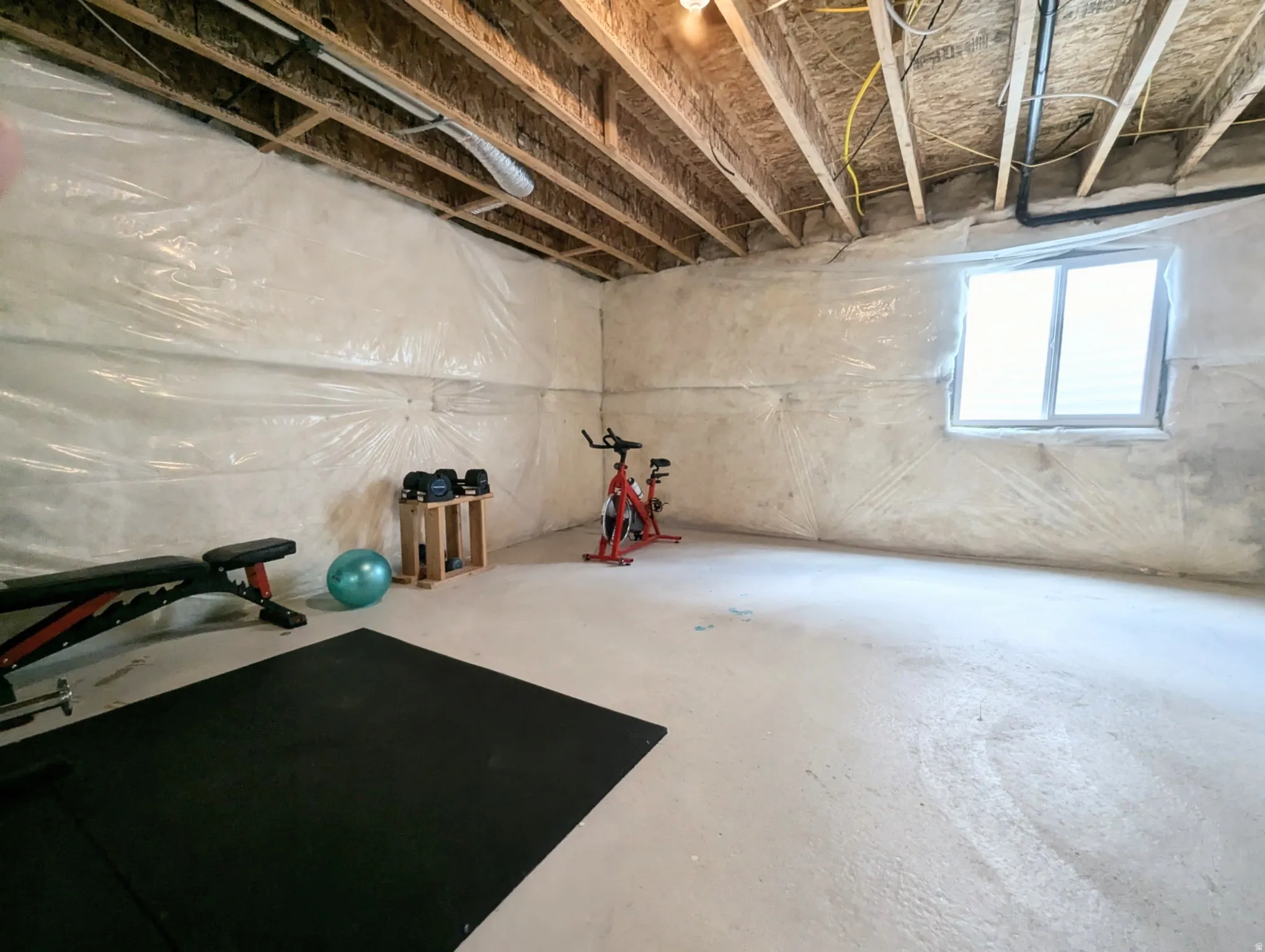 Unfinished basement space with exposed ceiling joists and subfloor, a single-pane window, and concrete flooring