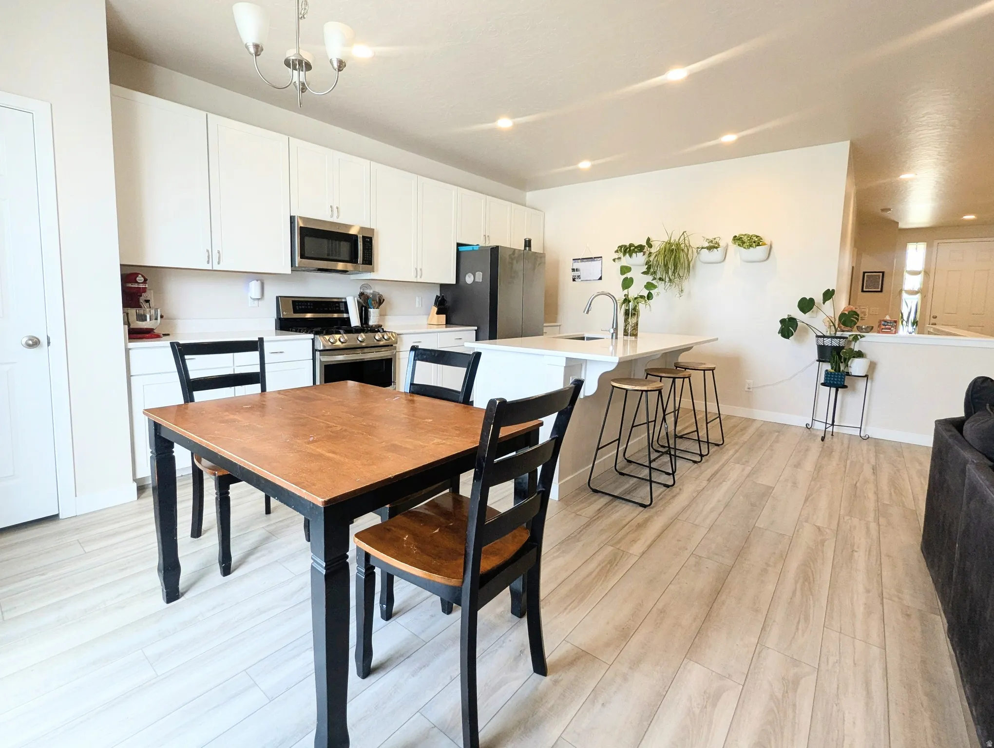 Open-concept kitchen and dining area featuring light wood-finish flooring, white cabinetry, stainless steel appliances, a kitchen island with seating, and recessed lighting