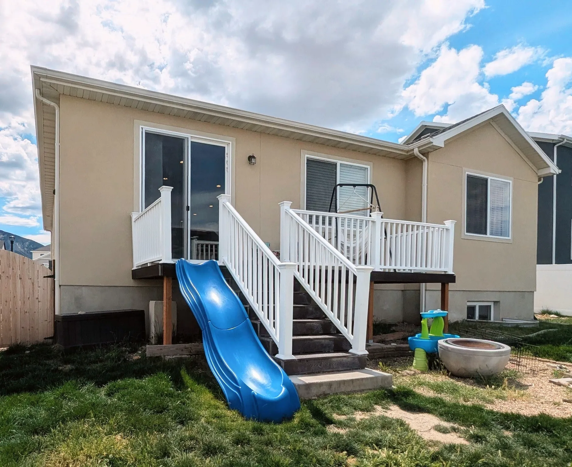 Rear exterior featuring a raised deck with white railings, sliding glass door access, and a concrete patio at ground level