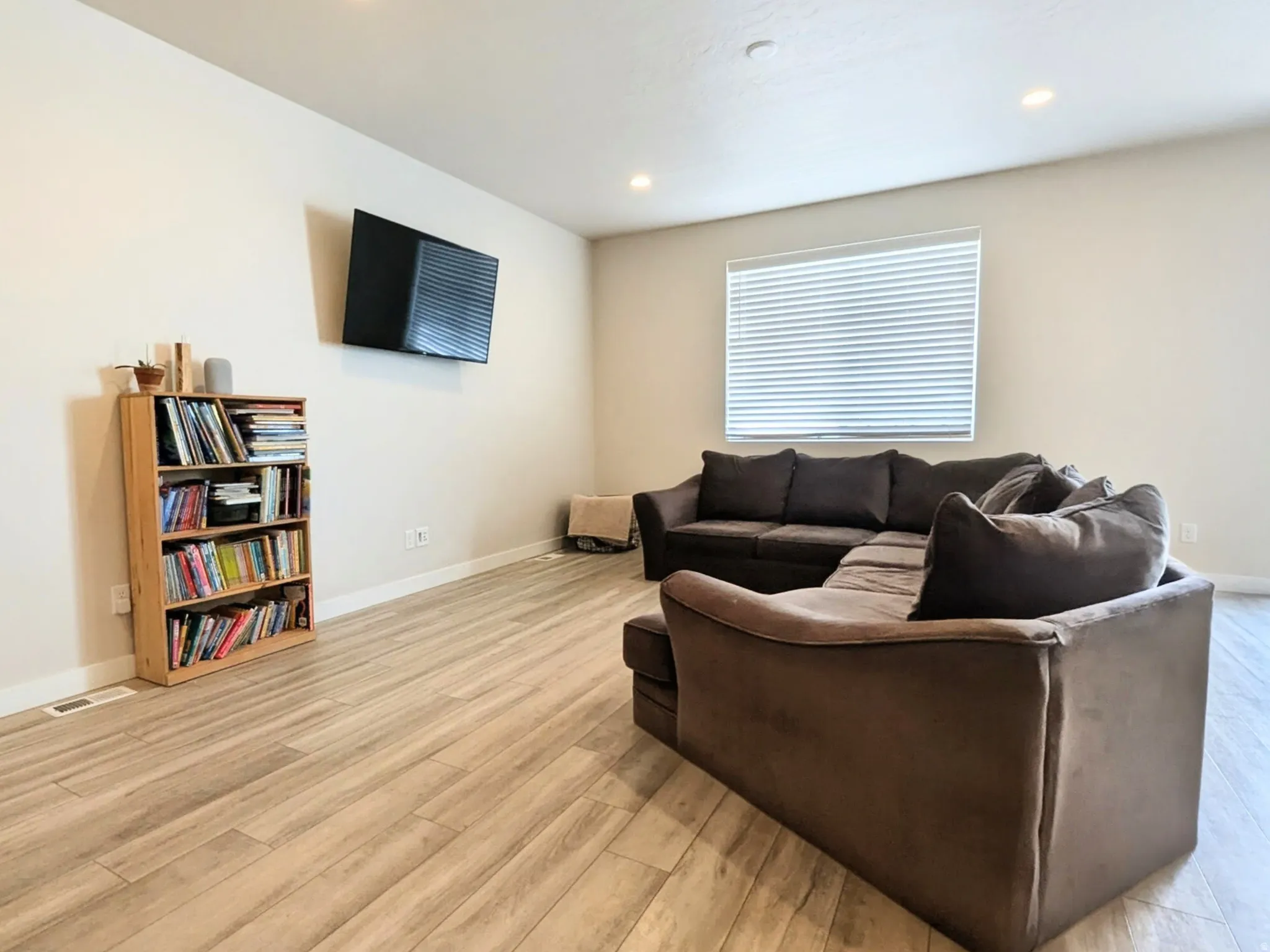 Spacious room featuring light-toned wood-finish flooring, recessed ceiling lighting, and a large window with blinds