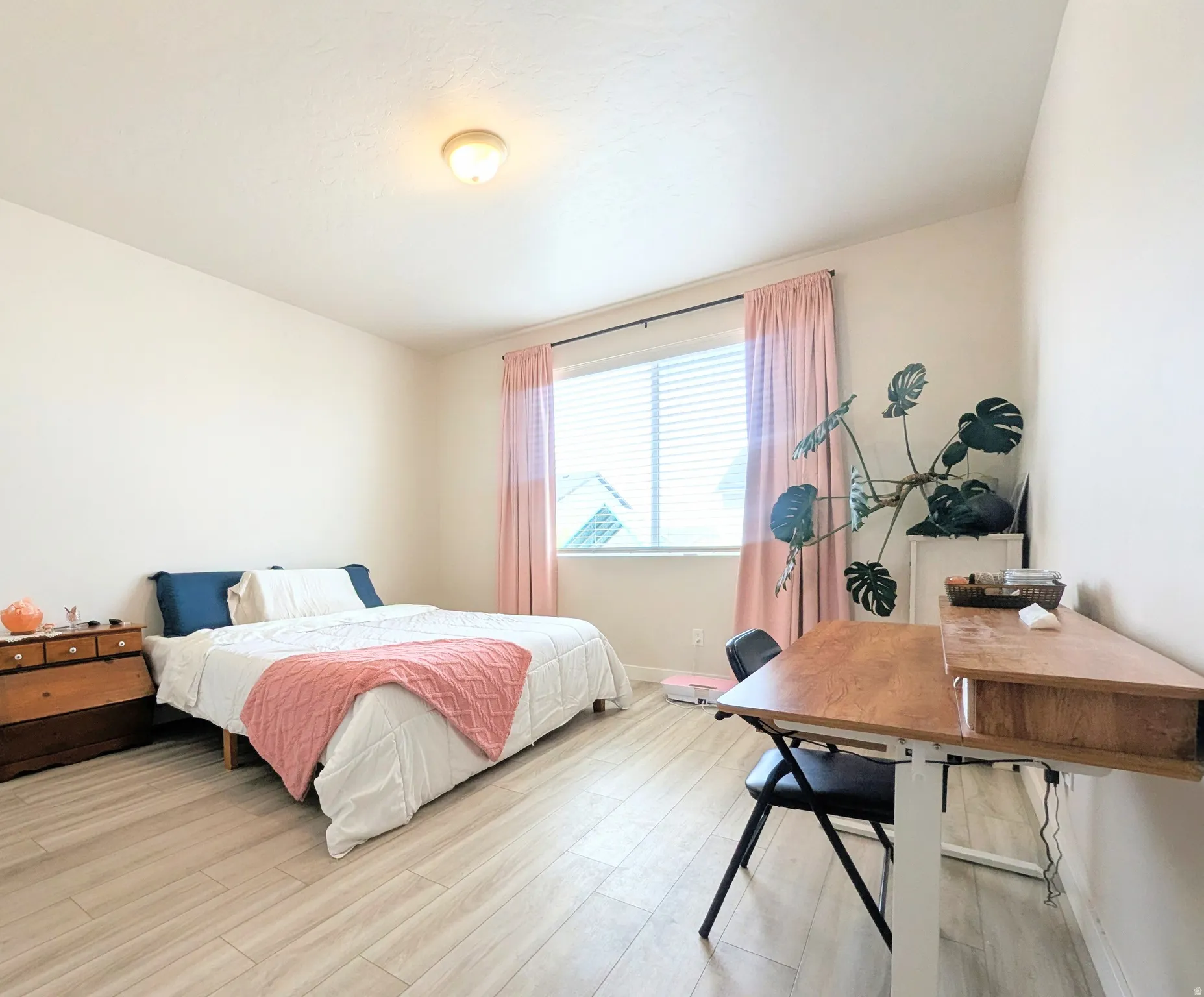 Spacious room featuring light-toned wood-finish flooring, a broad window with horizontal blinds, and a built-in overhead light fixture