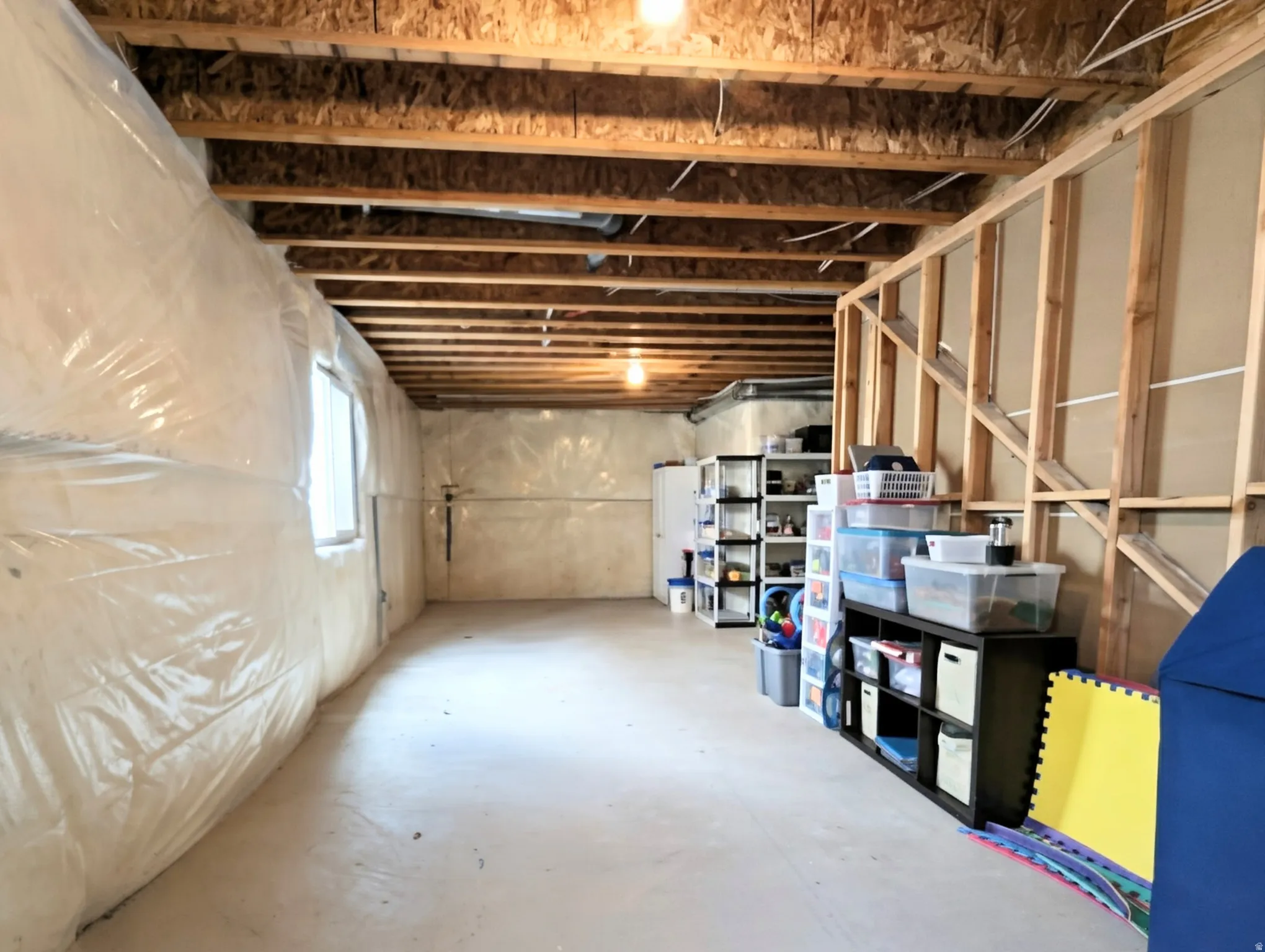 Unfinished basement featuring exposed wood ceiling joists and support beams, a concrete floor, and partial wall framing for future development
