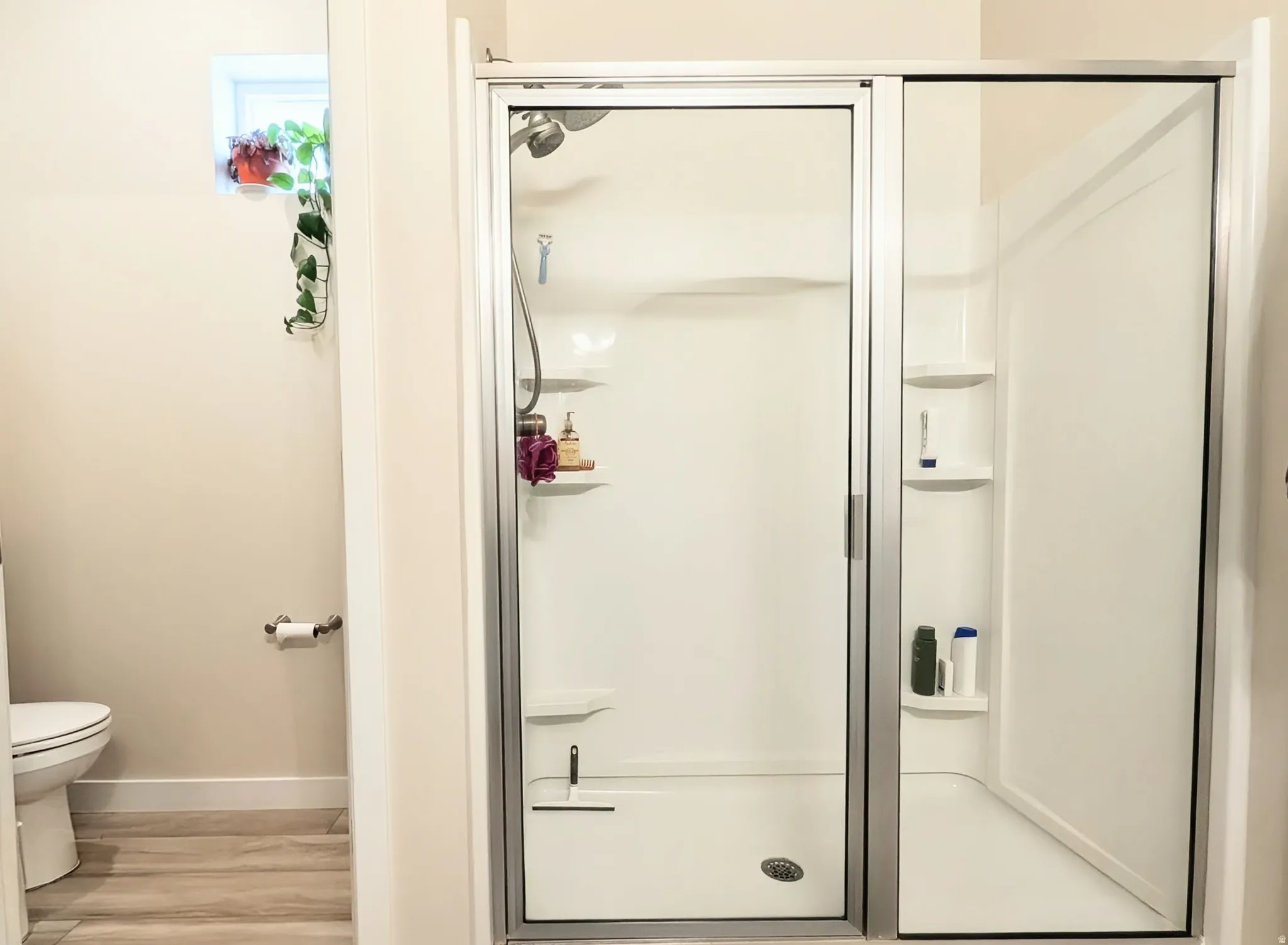 Glass-enclosed shower with a chrome showerhead and integrated shelving