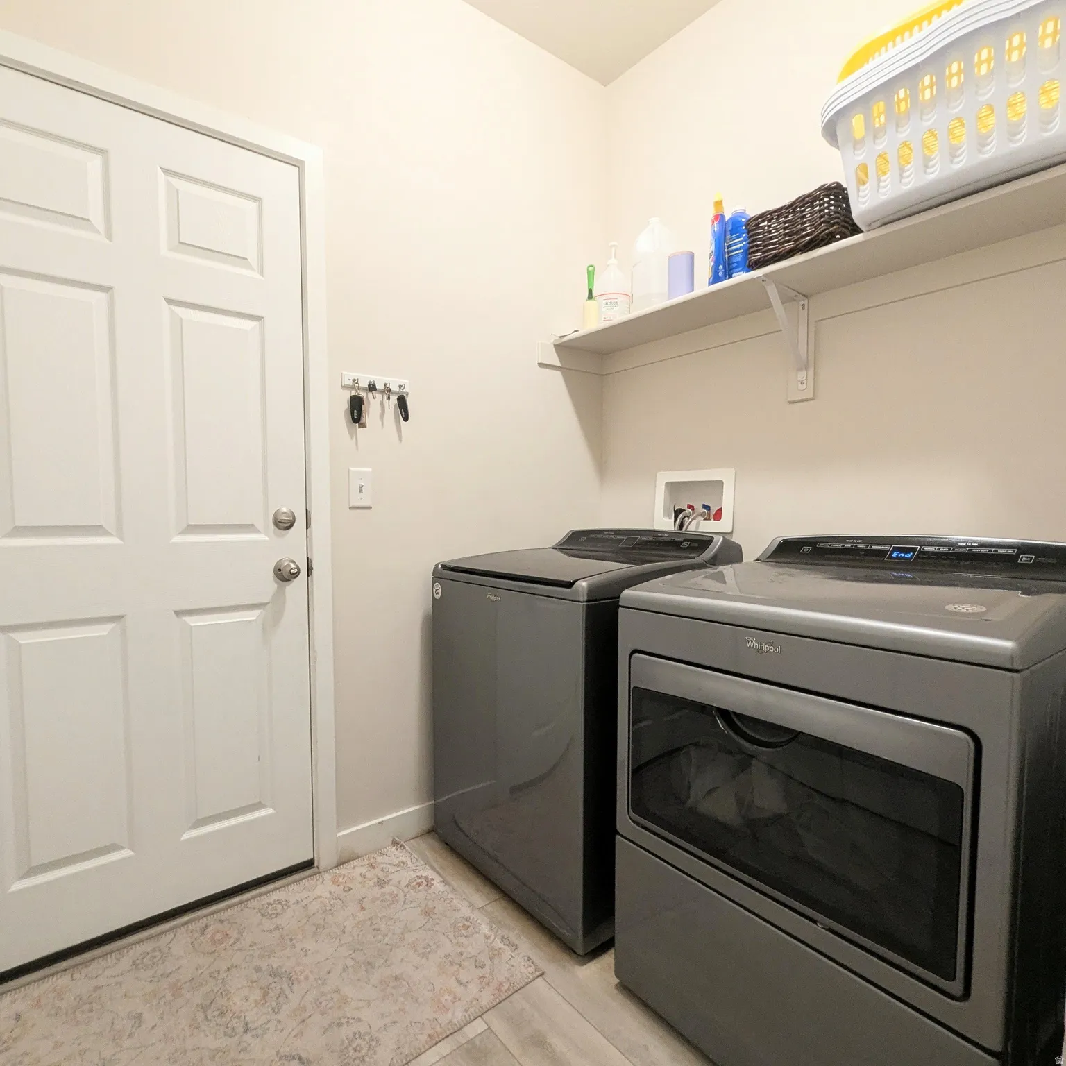 Dedicated laundry space featuring a white paneled door, light wood-finish flooring, and a wall-mounted shelving unit
