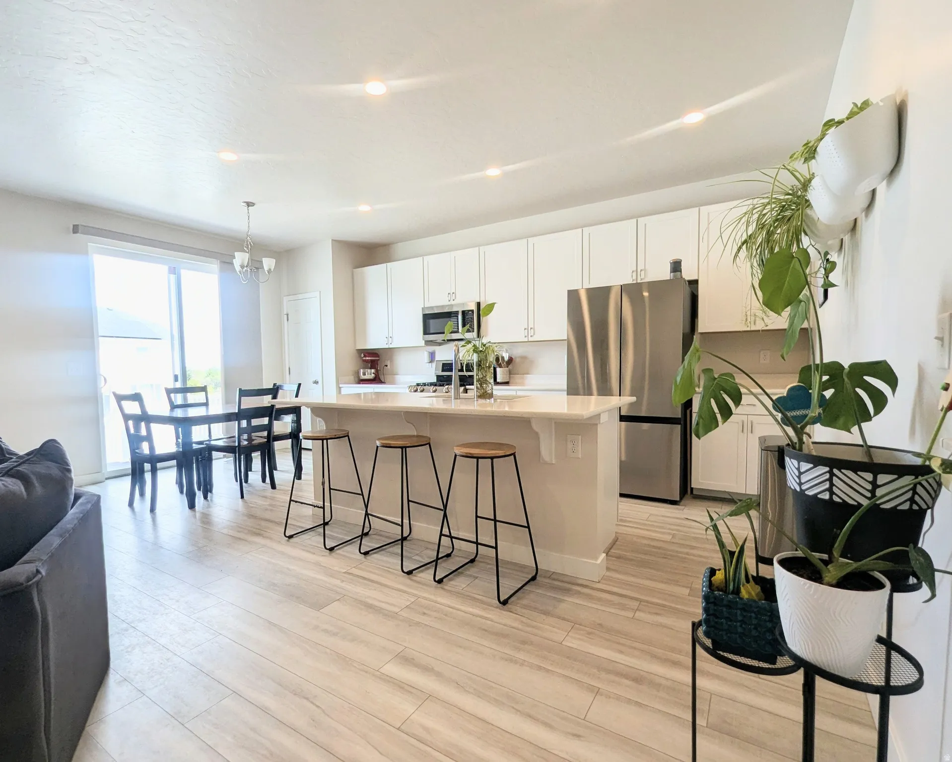 Open-concept living space featuring wood-finish flooring, a contemporary kitchen with white cabinetry, stainless steel appliances, a center island with bar seating, and recessed lighting