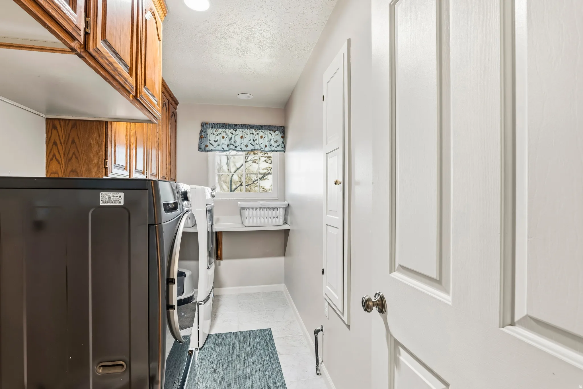 Dedicated laundry room featuring upper wood cabinetry, a built-in folding shelf, and a window for natural light