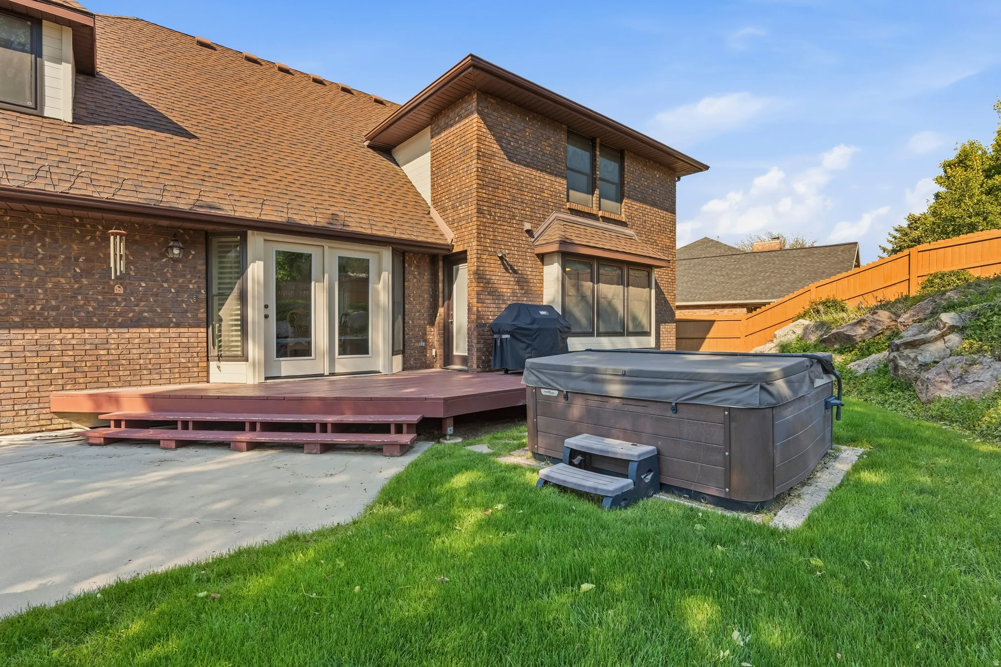 Expansive outdoor space featuring a hot tub, a large multi-level wood deck, concrete patio, and a manicured lawn