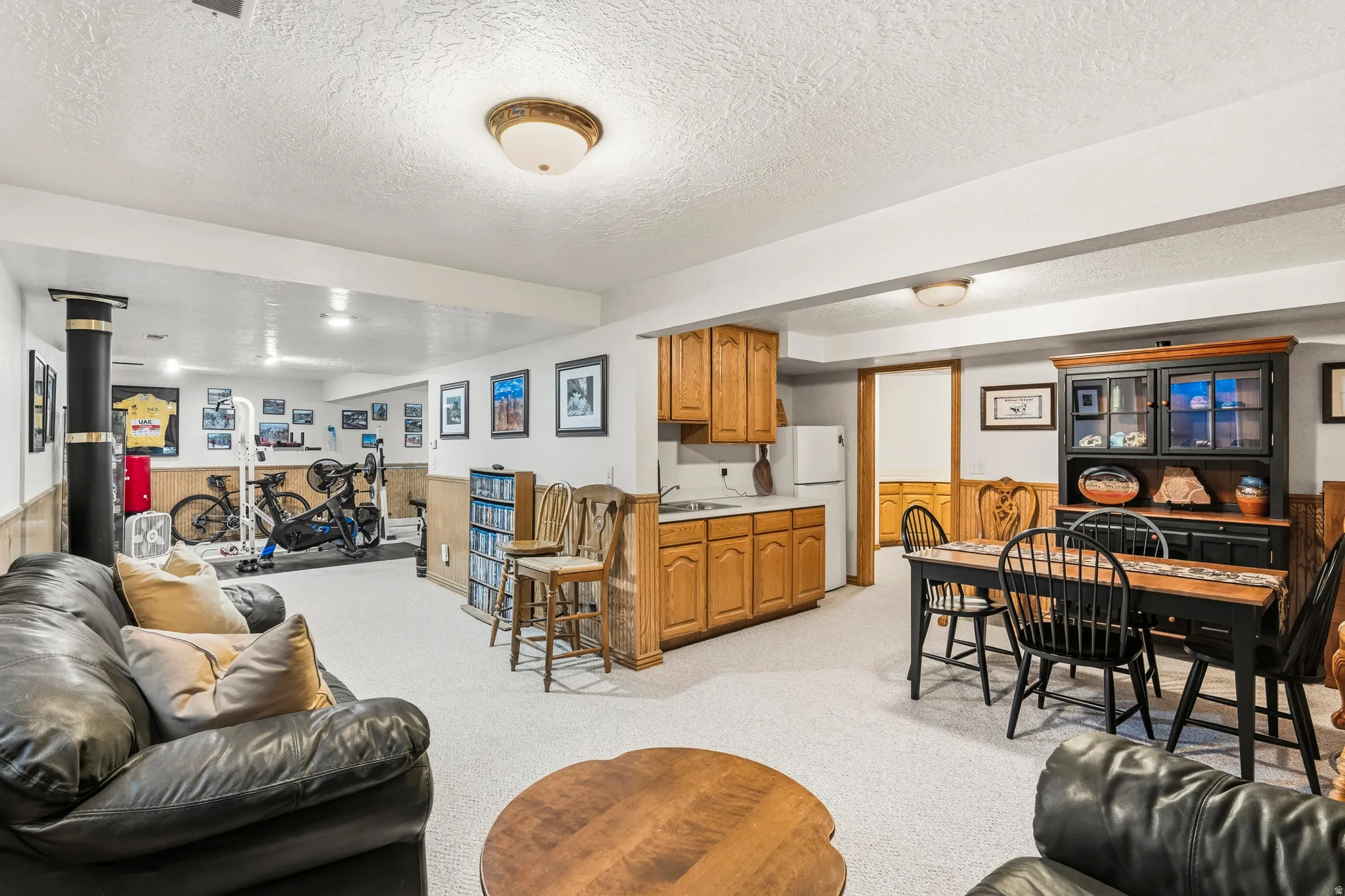 Spacious lower-level area featuring light-toned carpeting, a built-in kitchenette with wood cabinetry, and recessed lighting