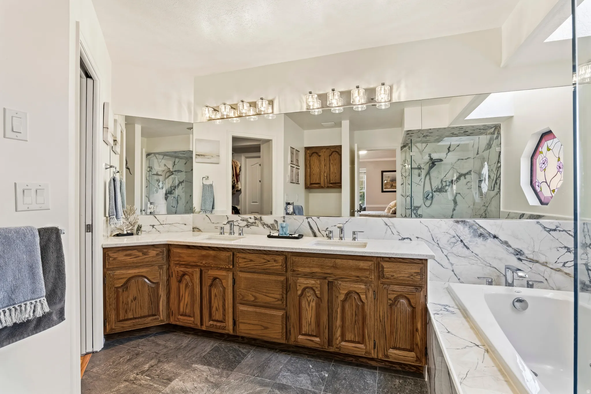 Dual basin vanity with wood cabinetry and white countertop, featuring a large mirror and overhead lighting