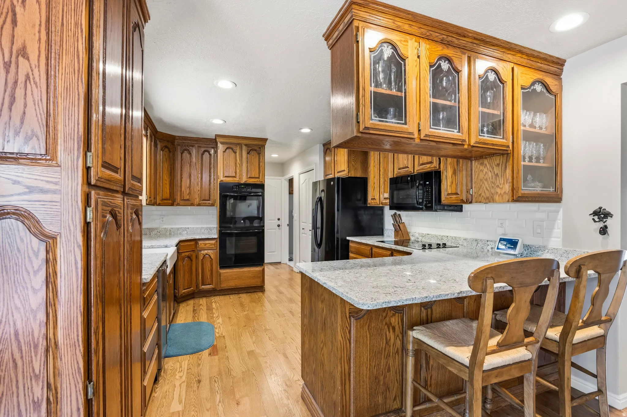 Kitchen featuring wood cabinetry, light-toned countertops, a full suite of black appliances, recessed lighting, and wood-finish flooring