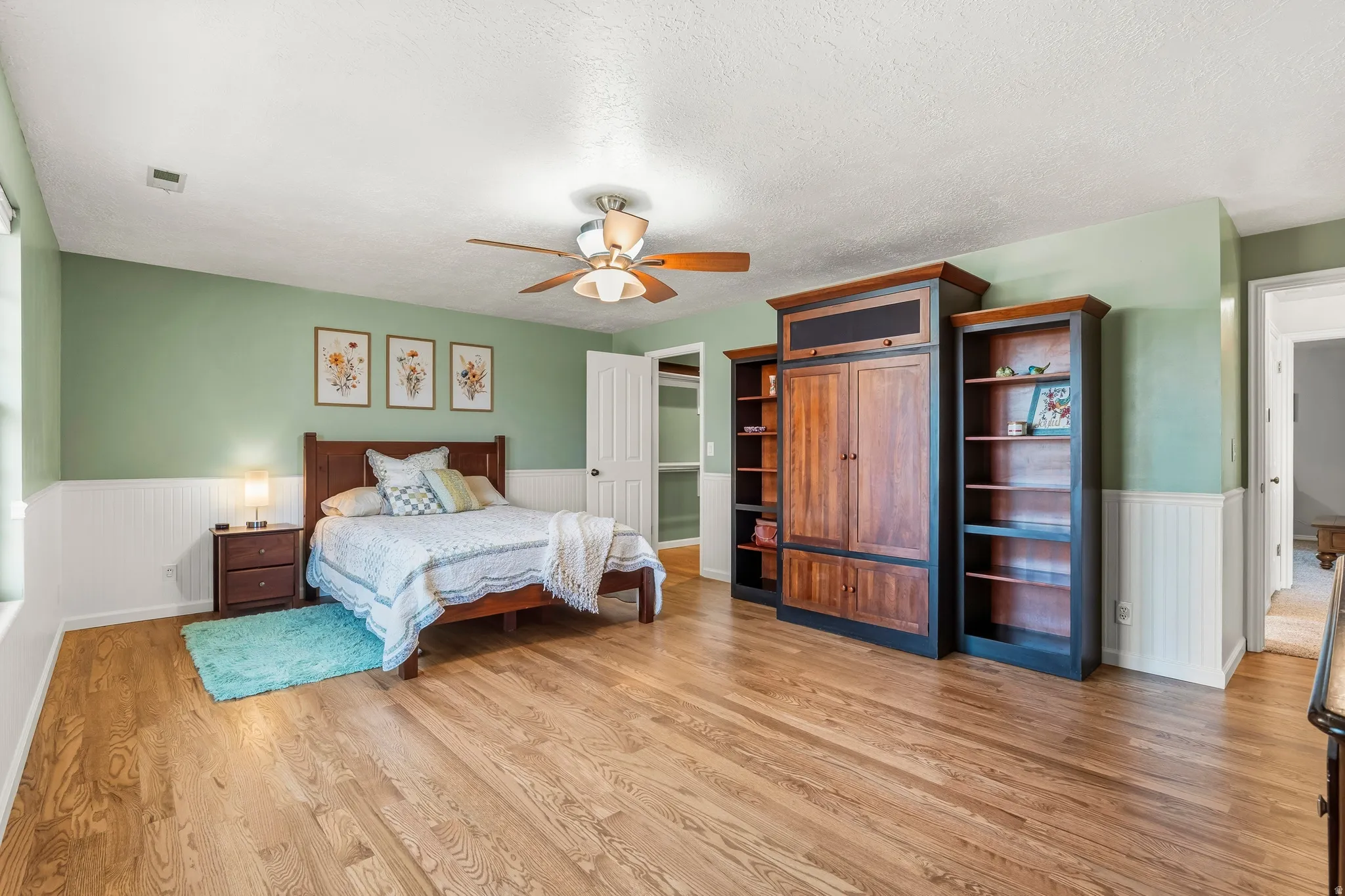 Spacious room featuring wood-finish flooring, half-wall beadboard paneling, and a ceiling fan with integrated lighting